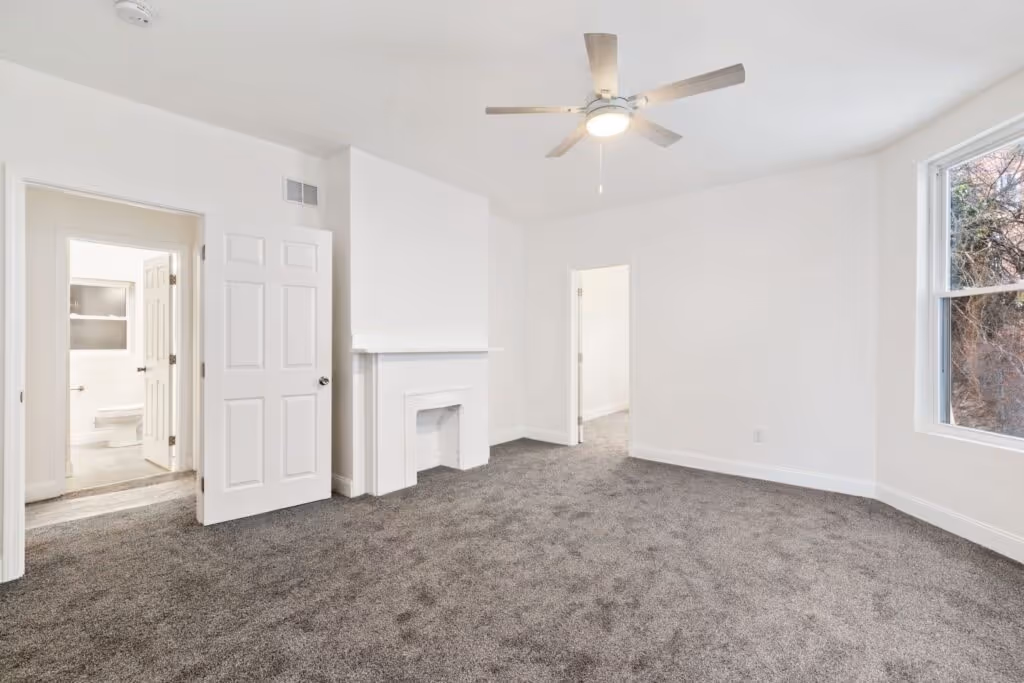 A finished, empty room at 240 Kennedy with new carpet, fresh white walls, and a ceiling fan